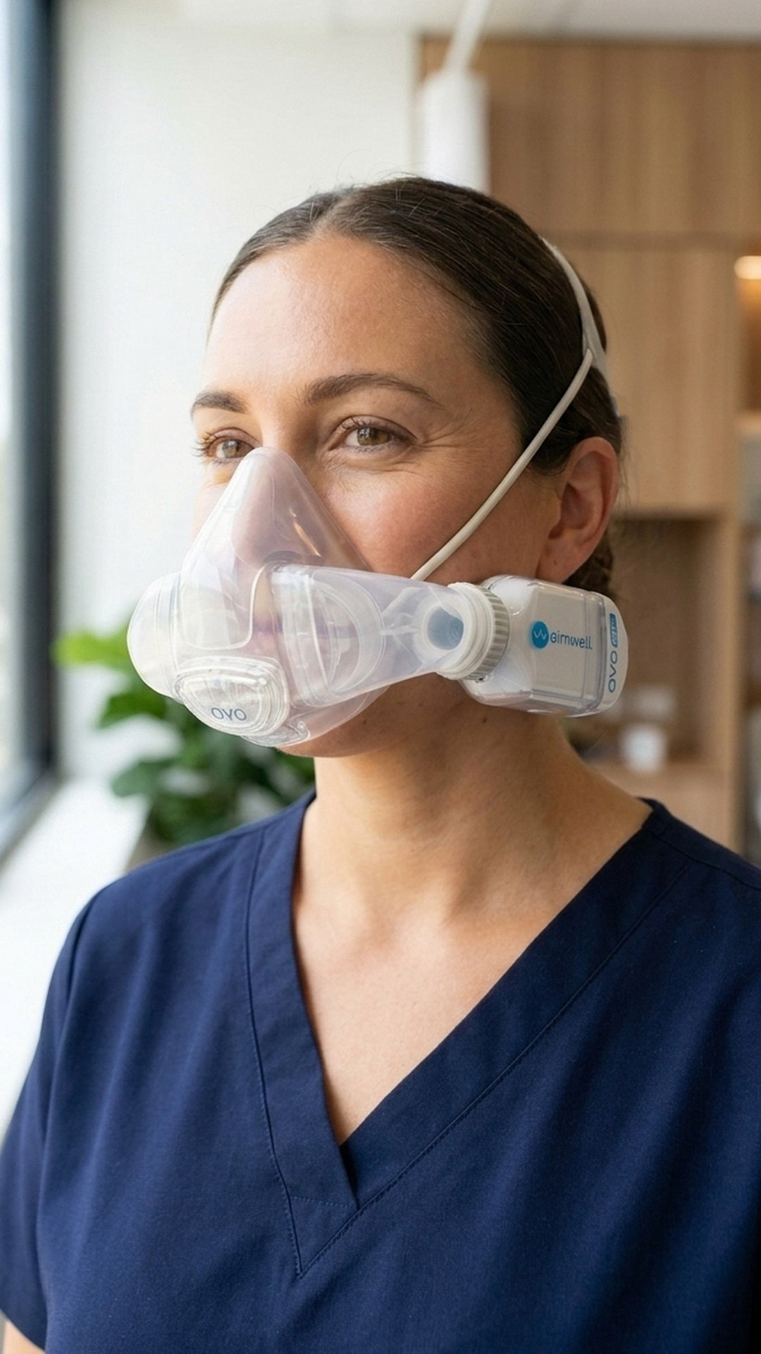 A nurse in navy scrubs wearing the AYO HC healthcare respirator in a bright hospital ward