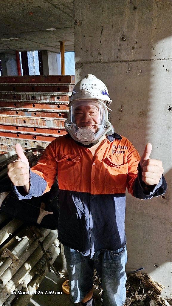 Construction worker giving two thumbs up while wearing an AYO WX full-face powered air-purifying respirator on a concrete building site