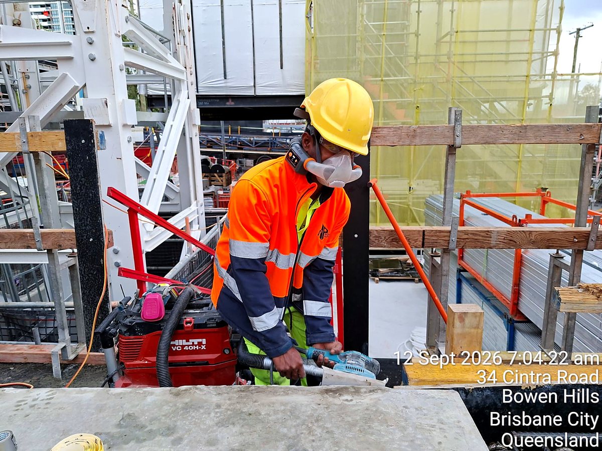 Worker in hi-vis sanding concrete with an extraction sander while wearing an AYO WX half-face powered respirator, Brisbane